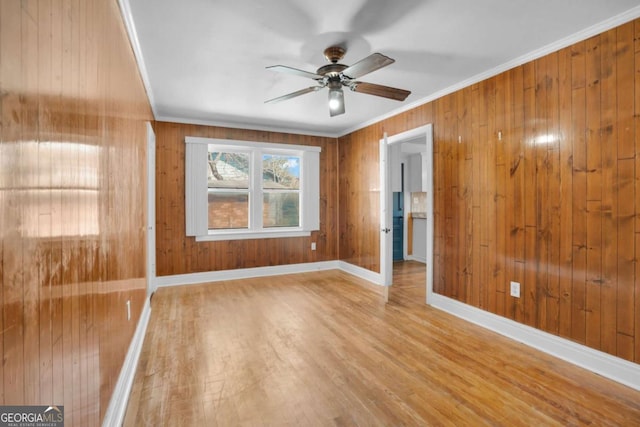 spare room with baseboards, wood walls, ornamental molding, wood finished floors, and a ceiling fan