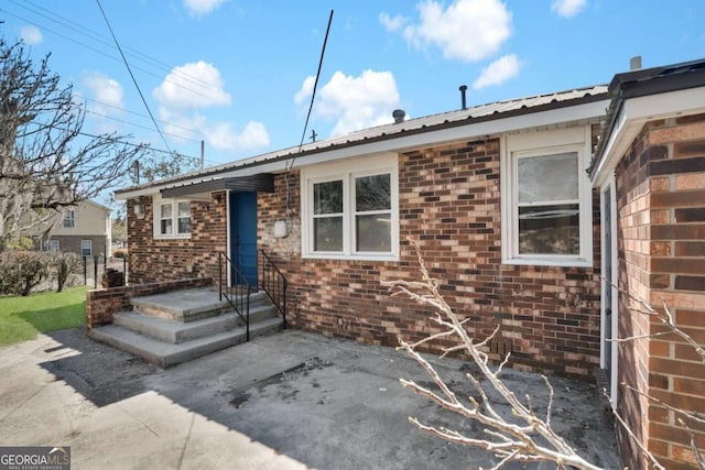 ranch-style house with metal roof, a patio, and brick siding