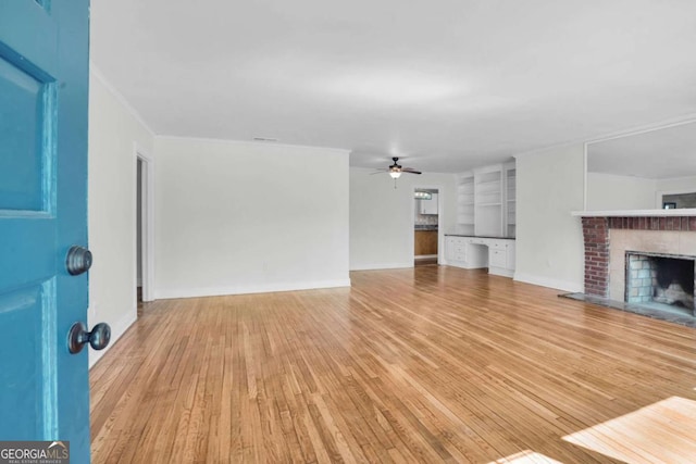 unfurnished living room with wood finished floors, baseboards, a fireplace, ornamental molding, and ceiling fan