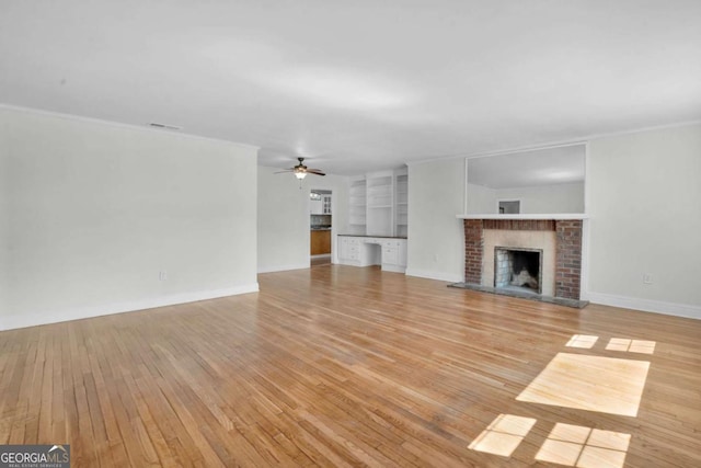 unfurnished living room featuring light wood-style floors, crown molding, baseboards, a brick fireplace, and ceiling fan