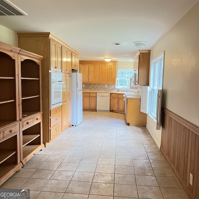 kitchen with white appliances, light tile patterned flooring, light countertops, and a wainscoted wall