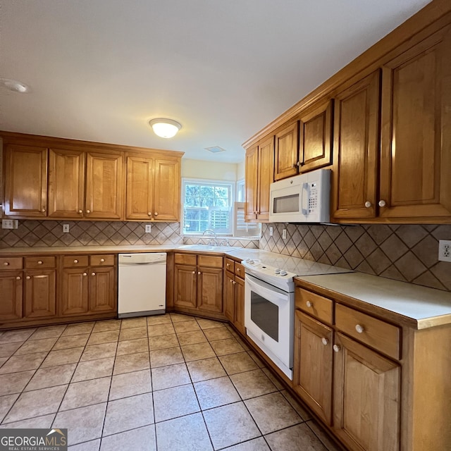 kitchen with decorative backsplash, light tile patterned flooring, brown cabinetry, white appliances, and a sink