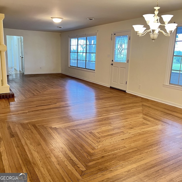 unfurnished living room with parquet flooring, a notable chandelier, baseboards, and ornate columns