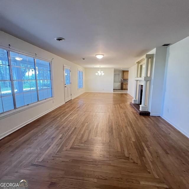 unfurnished living room featuring a notable chandelier, a fireplace with raised hearth, visible vents, and baseboards