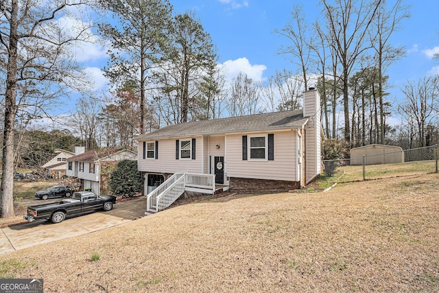 split foyer home with a front yard, fence, roof with shingles, driveway, and a chimney