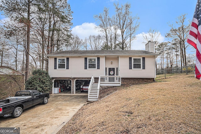 split foyer home with fence, concrete driveway, a front yard, a carport, and a chimney