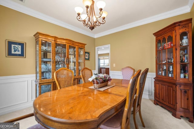 dining room featuring crown molding, a notable chandelier, wainscoting, and light carpet