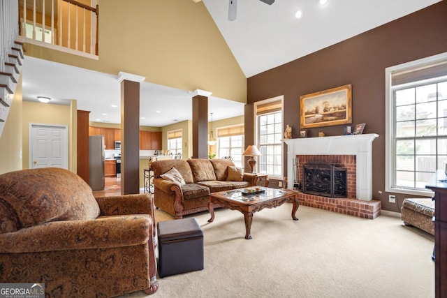 carpeted living area with baseboards, ceiling fan, decorative columns, a fireplace, and high vaulted ceiling