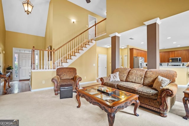 living area featuring a high ceiling, stairs, baseboards, and decorative columns