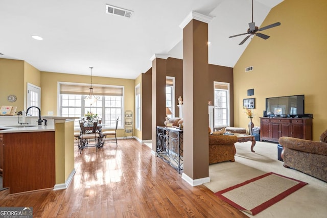 living room featuring wood finished floors, visible vents, baseboards, a high ceiling, and ceiling fan