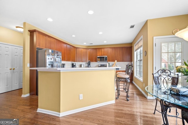 kitchen featuring light wood finished floors, recessed lighting, a kitchen island with sink, stainless steel appliances, and light countertops