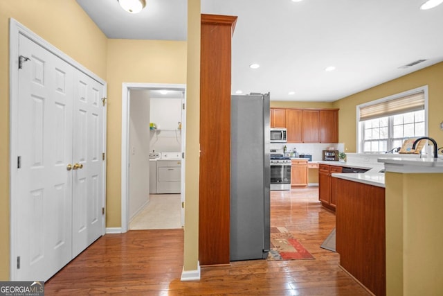 kitchen with visible vents, washing machine and clothes dryer, stainless steel appliances, light countertops, and light wood-style floors