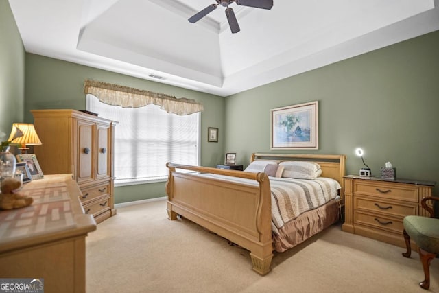 bedroom featuring light carpet, visible vents, ceiling fan, and a tray ceiling