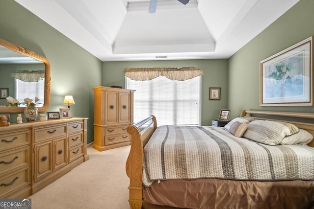 bedroom with light carpet, visible vents, a raised ceiling, and a ceiling fan