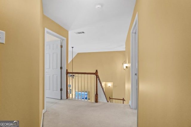 hallway with an upstairs landing, visible vents, and carpet flooring