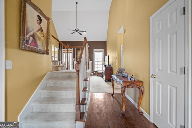 staircase featuring baseboards, high vaulted ceiling, and wood finished floors