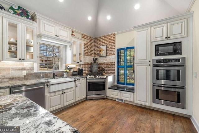 kitchen featuring a sink, backsplash, wood finished floors, appliances with stainless steel finishes, and lofted ceiling