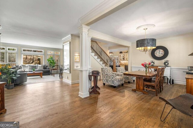interior space featuring wood finished floors, ornate columns, an inviting chandelier, wainscoting, and crown molding