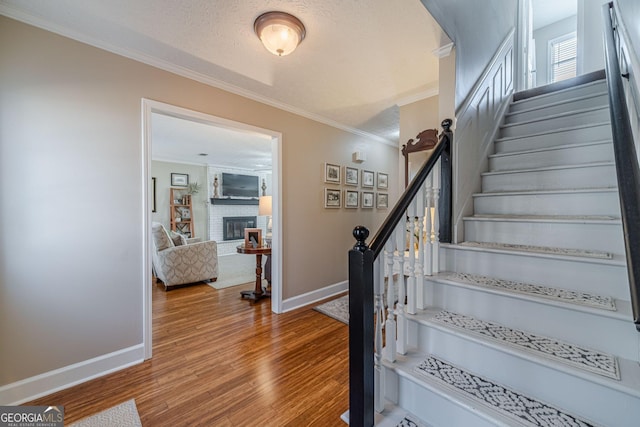 stairway featuring a fireplace, a textured ceiling, wood finished floors, and ornamental molding