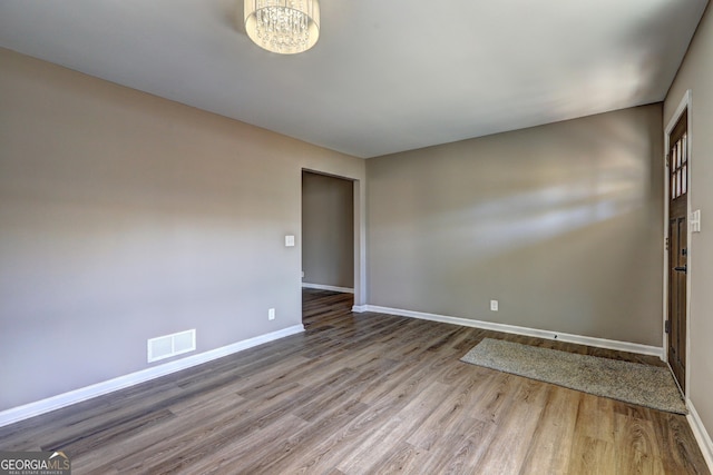 empty room with wood finished floors, visible vents, a chandelier, and baseboards