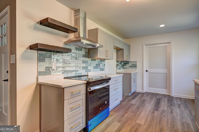 kitchen featuring light wood finished floors, tasteful backsplash, wall chimney range hood, light countertops, and stainless steel electric range