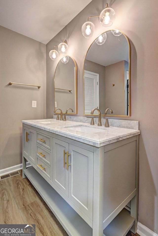 full bathroom with double vanity, visible vents, wood finished floors, and a sink