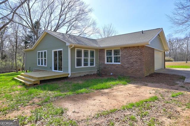 rear view of property featuring a deck, concrete driveway, an attached garage, a shingled roof, and brick siding