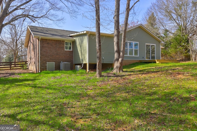 back of property featuring fence, brick siding, central AC, and a lawn