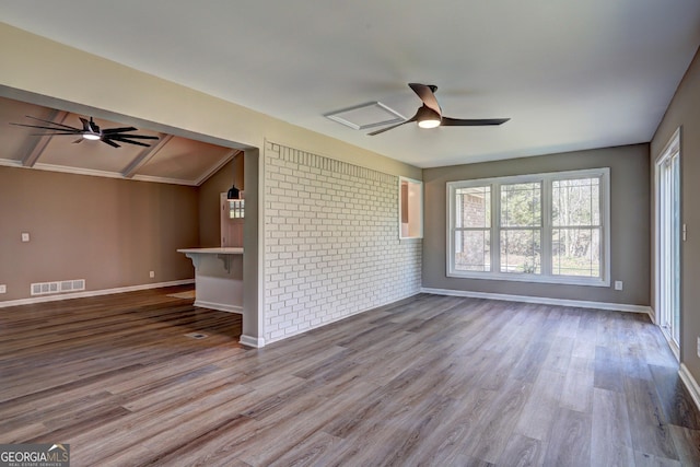 spare room featuring wood finished floors, visible vents, brick wall, and ceiling fan