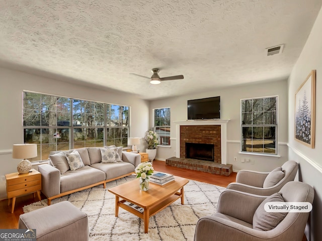 living room with visible vents, ceiling fan, a fireplace, wood finished floors, and a textured ceiling