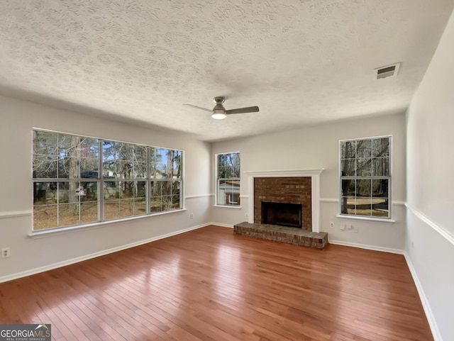 unfurnished living room with a ceiling fan, hardwood / wood-style flooring, a fireplace, and visible vents