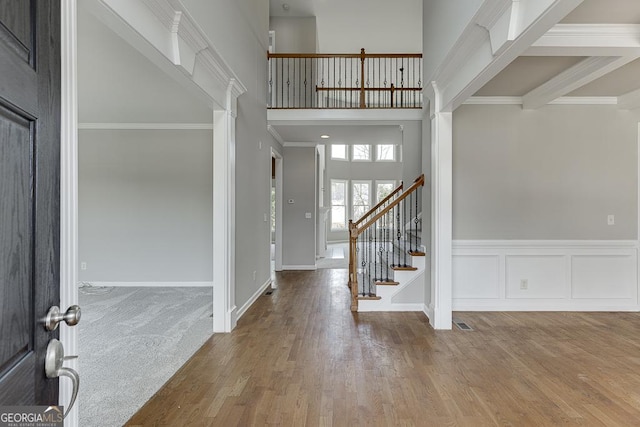 entrance foyer with wood finished floors, ornamental molding, stairs, a towering ceiling, and wainscoting