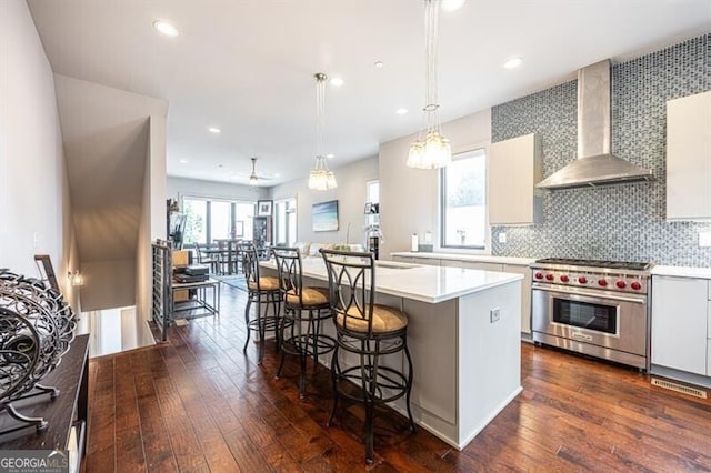 kitchen featuring luxury range, light countertops, dark wood-type flooring, a kitchen breakfast bar, and wall chimney exhaust hood