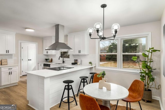 kitchen featuring light wood finished floors, a sink, light countertops, dishwasher, and wall chimney exhaust hood