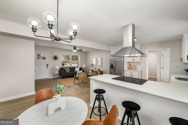 kitchen with island exhaust hood, wood finished floors, stainless steel fridge, a peninsula, and black electric stovetop