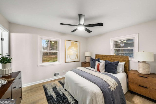 bedroom with light wood finished floors, visible vents, multiple windows, and baseboards