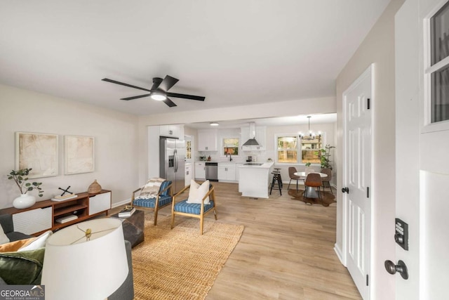 living area featuring light wood-style flooring and ceiling fan with notable chandelier