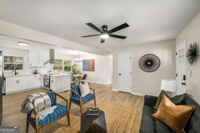 living room featuring ceiling fan with notable chandelier, baseboards, and light wood-type flooring