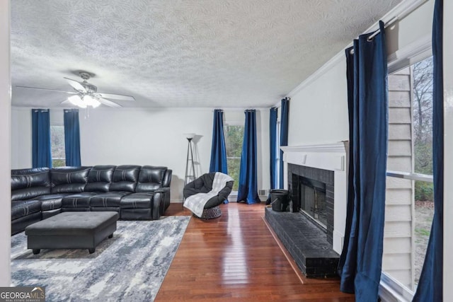 living room featuring a fireplace, a textured ceiling, a ceiling fan, and wood finished floors