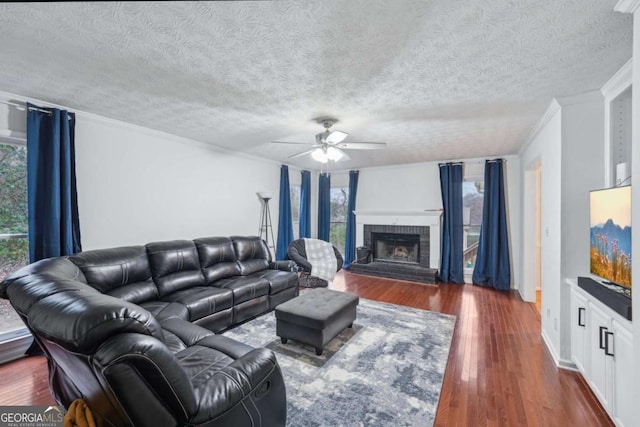 living room featuring dark wood-type flooring, ornamental molding, a fireplace, a textured ceiling, and a ceiling fan