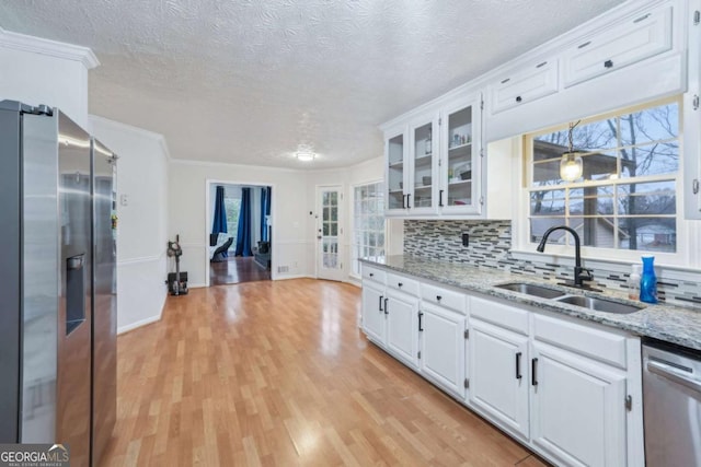 kitchen with appliances with stainless steel finishes, white cabinetry, light wood-style floors, and a sink