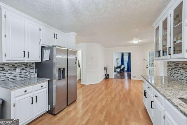 kitchen featuring backsplash, glass insert cabinets, light wood-style flooring, stainless steel refrigerator with ice dispenser, and white cabinets