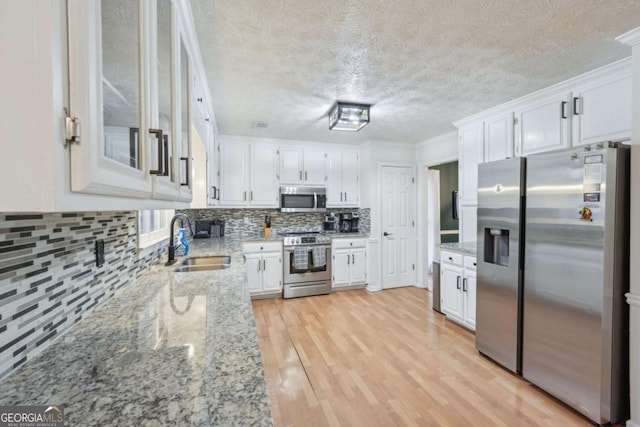 kitchen featuring white cabinets, stainless steel appliances, light wood-style floors, and a sink