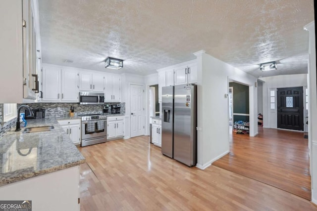 kitchen with a sink, light wood-type flooring, appliances with stainless steel finishes, and white cabinets