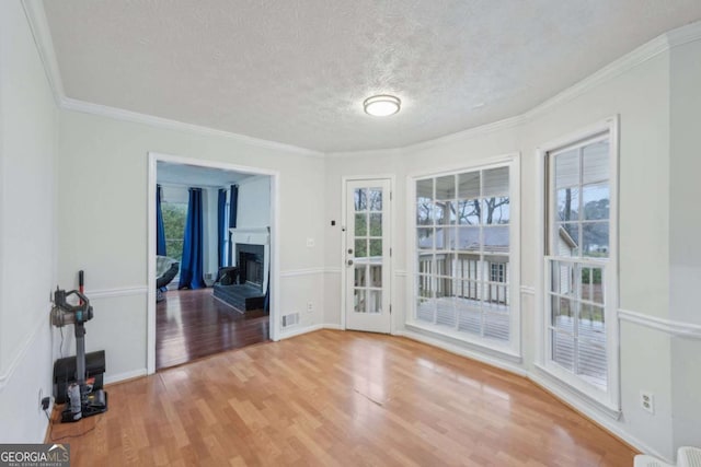 interior space featuring a fireplace with raised hearth, a textured ceiling, wood finished floors, crown molding, and baseboards