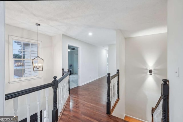 corridor featuring baseboards, dark wood-type flooring, a textured ceiling, a notable chandelier, and an upstairs landing