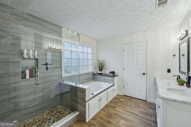 bathroom with visible vents, wood finish floors, a sink, a shower stall, and a garden tub