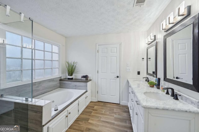 full bathroom featuring visible vents, wood tiled floor, a sink, a textured ceiling, and a garden tub