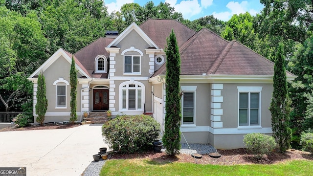 traditional-style home with stucco siding, french doors, and roof with shingles