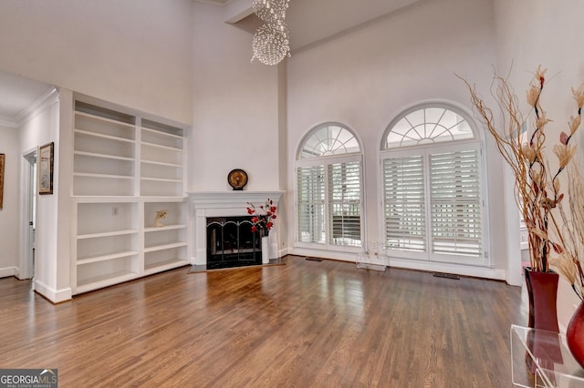 unfurnished living room featuring wood finished floors, a fireplace, a chandelier, baseboards, and a towering ceiling